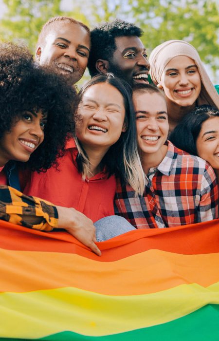Happy diverse people holding lgbt rainbow flag outdoors - Diversity concept - Soft focus on Asian young woman face